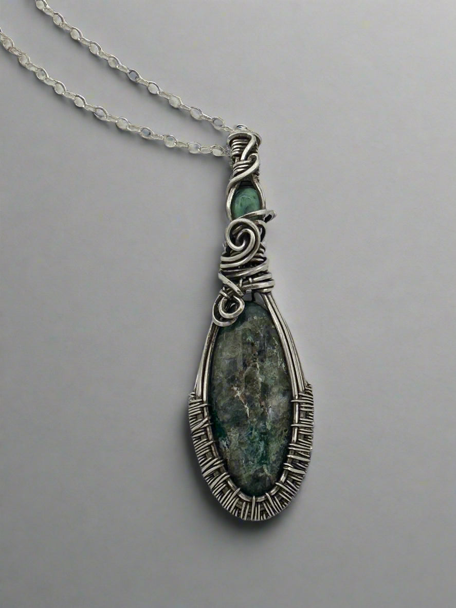 Silver pendant with green stone on a chain against a light gray background
