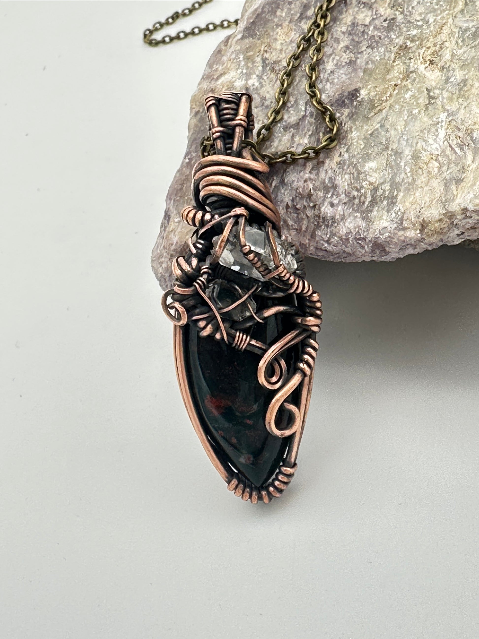 Copper and black stone pendant on a chain, placed on a rock with a light gray background