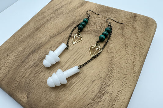 Pair of earplugs with green beads and gold geometric charms on a wooden surface