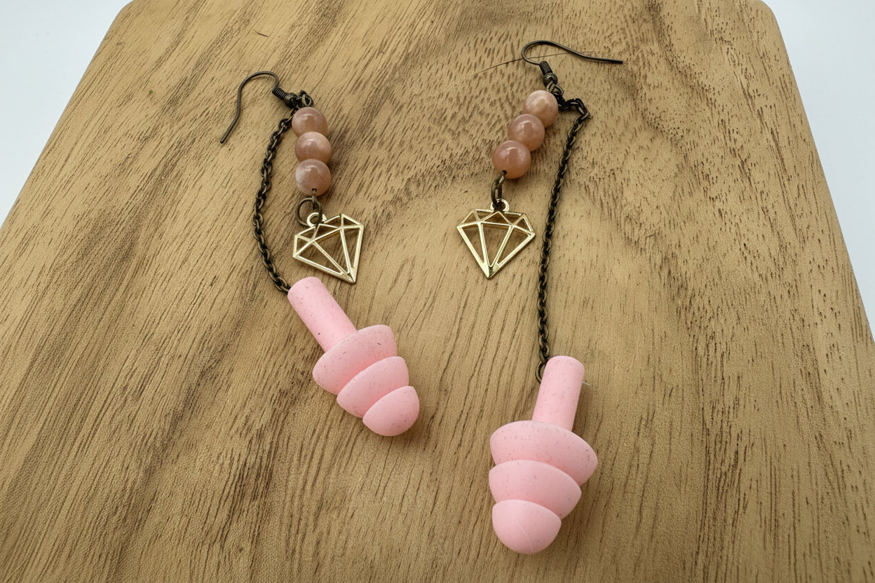 Pink earplugs with geometric and beaded straps on a wooden surface
