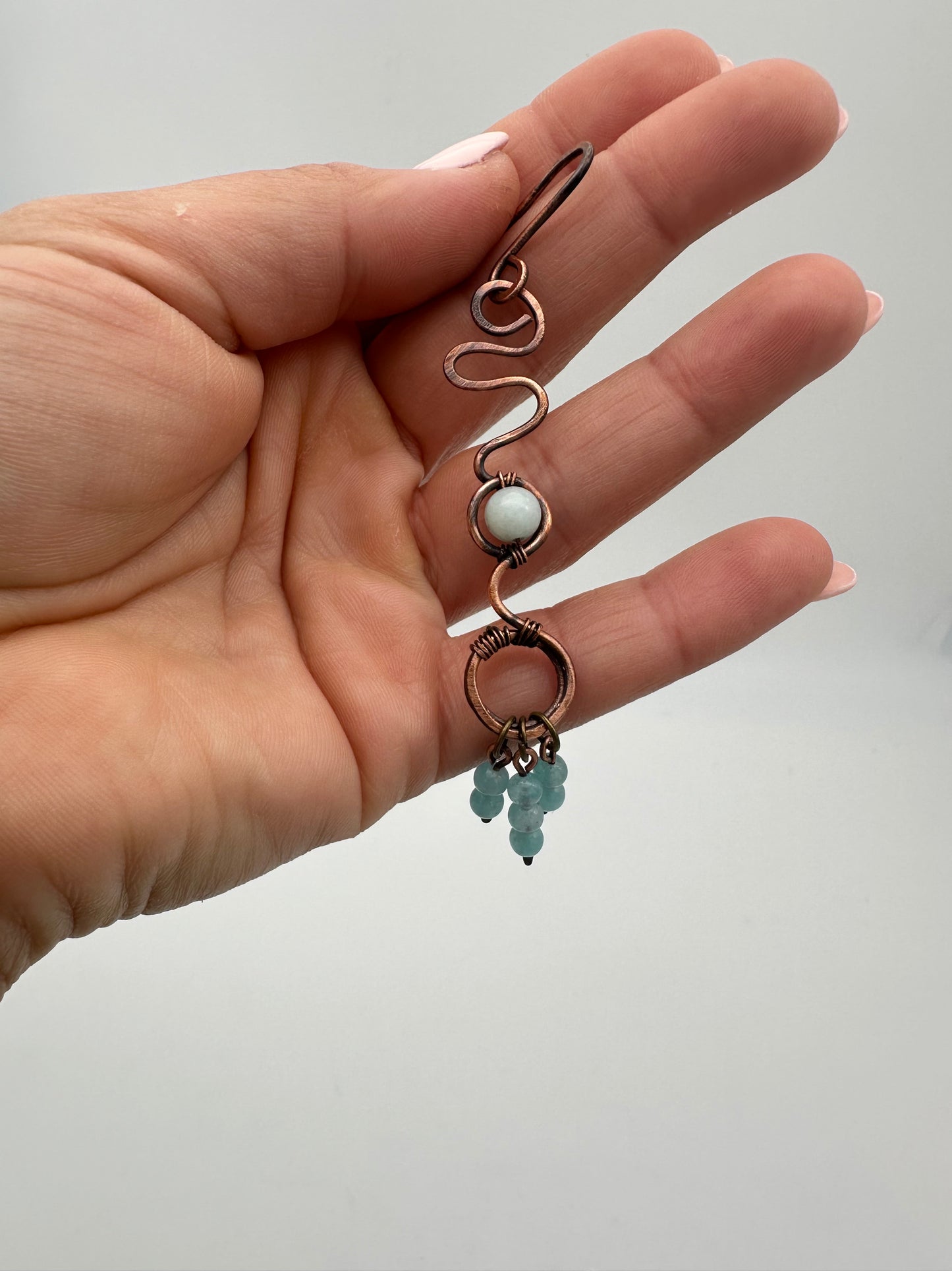 Hand holding two wire-wrapped gemstone rings against a plain background