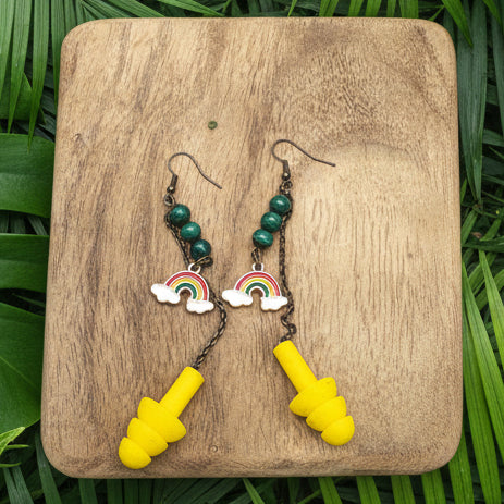 Pair of yellow earplugs and a set of earrings with rainbow and cloud charms on a wooden surface.