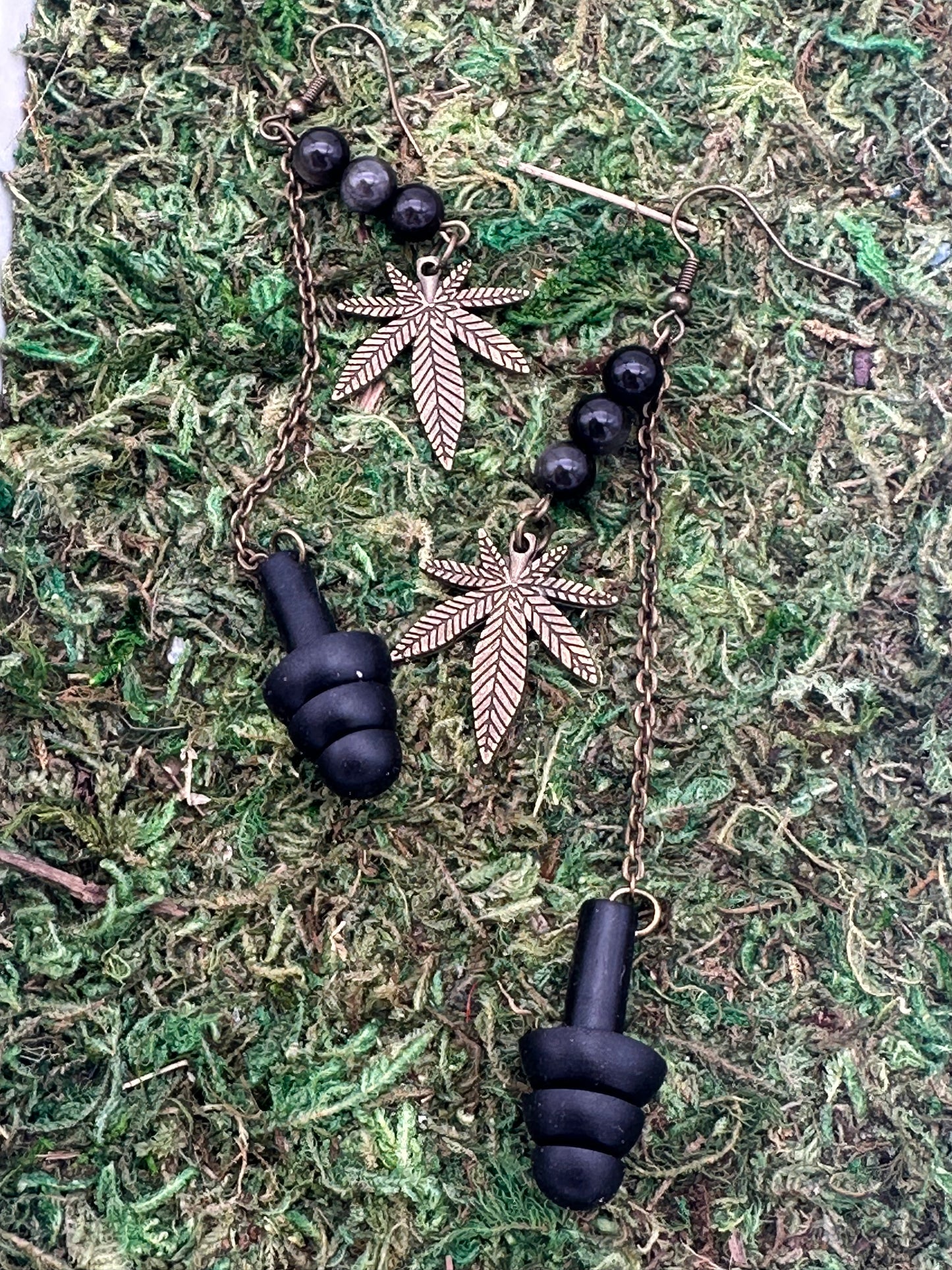 Black earplugs and gold leaf-shaped earrings on a green moss background