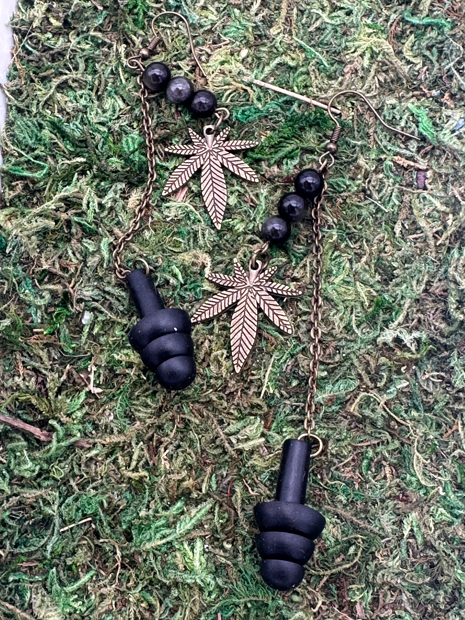 Black earplugs and gold leaf-shaped earrings on a green moss background