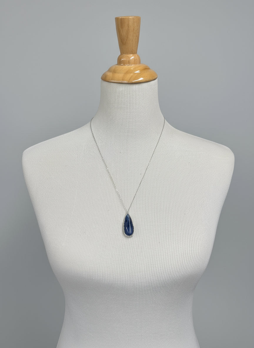 White dress on a mannequin with a blue brooch against a patterned fabric background