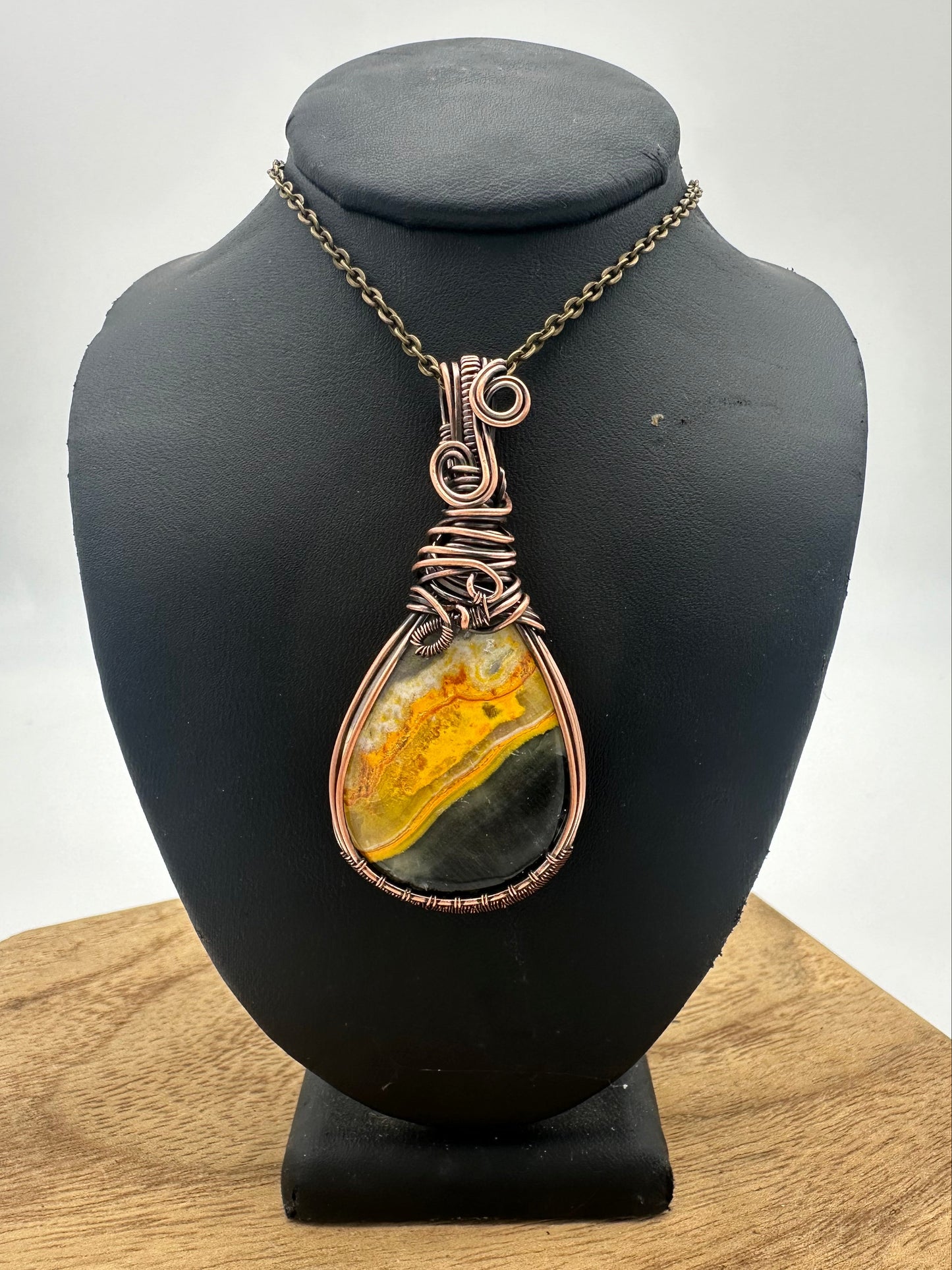 Jewelry pendant with a yellow and green stone on a black mannequin head against a white background