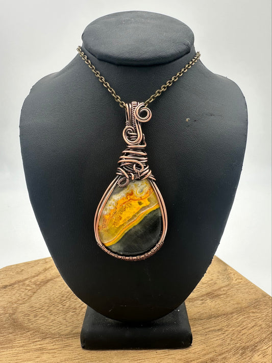 Jewelry pendant with a yellow and green stone on a black mannequin head against a white background