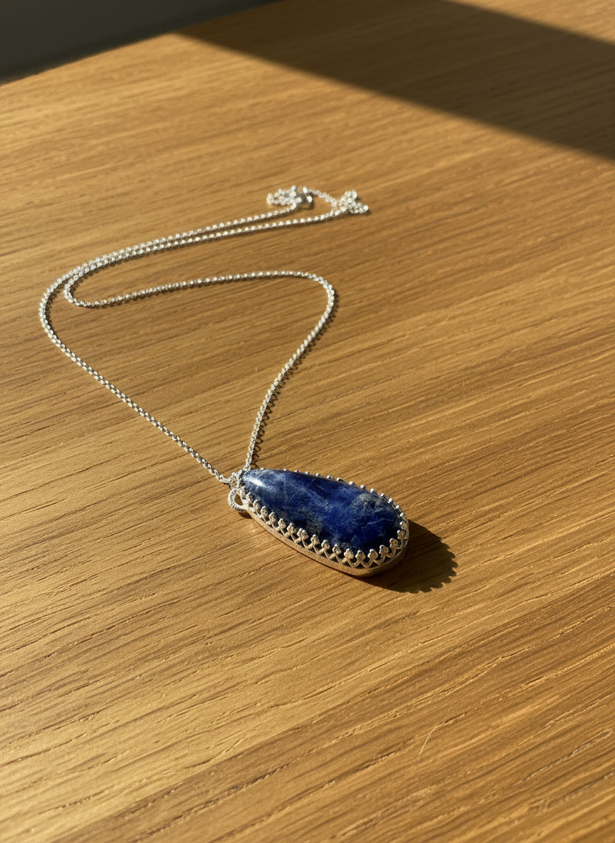 Teardrop-shaped blue pendant on a silver chain against a white background