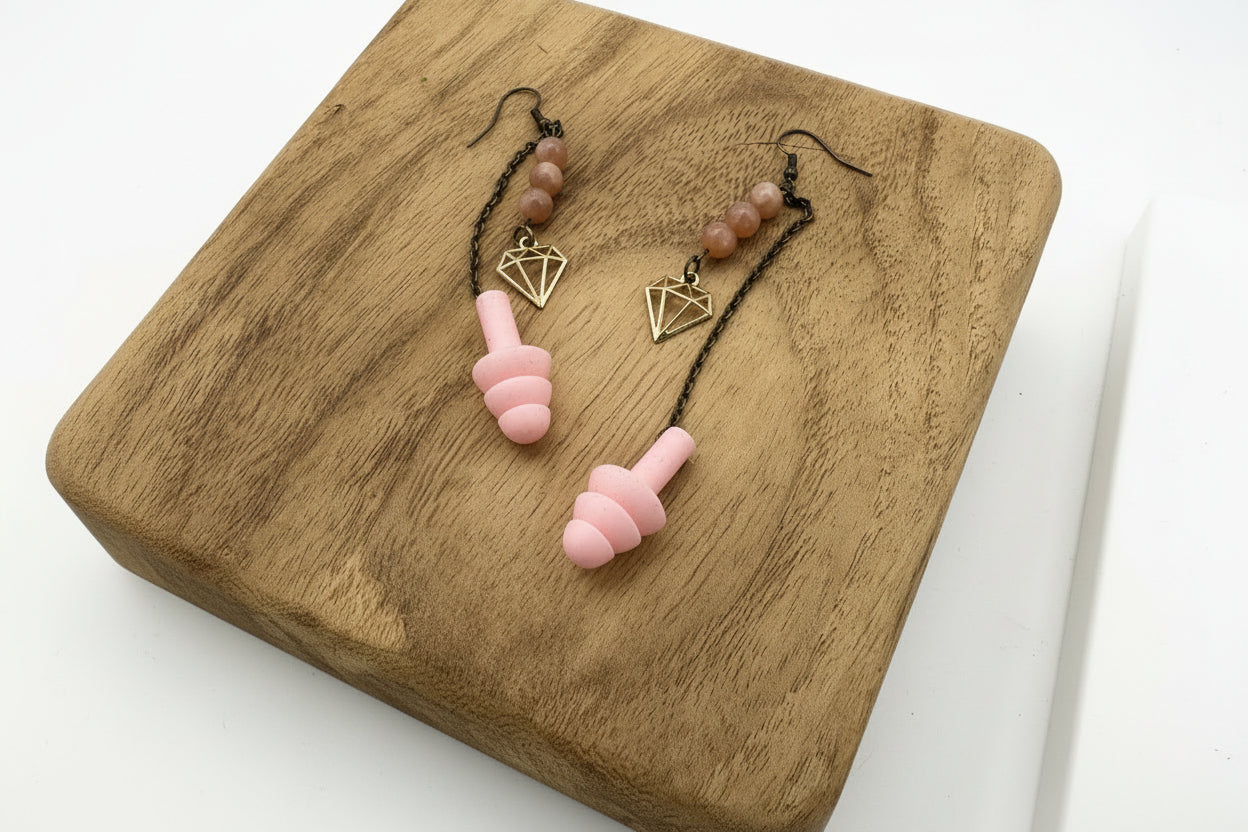 Pink earplugs and gold necklaces on a wooden surface