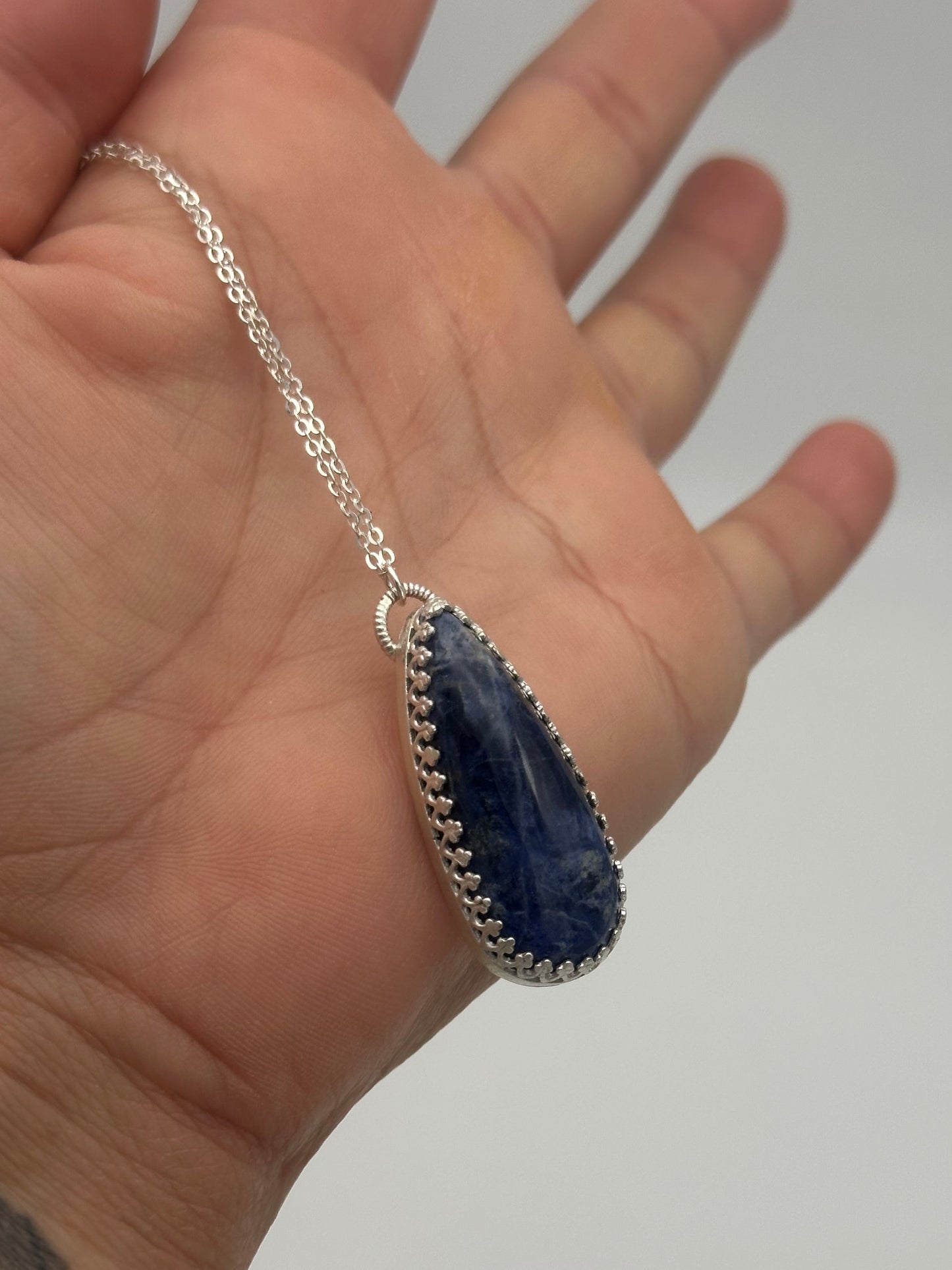 Hand wearing a silver bracelet with a blue stone on a plain background