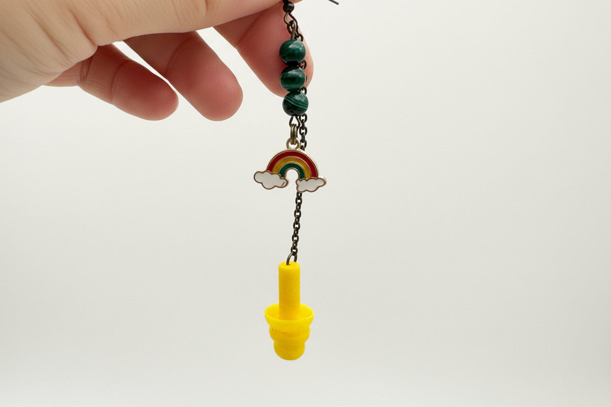Hand holding a small decorative item with beads and a yellow cap against a plain background