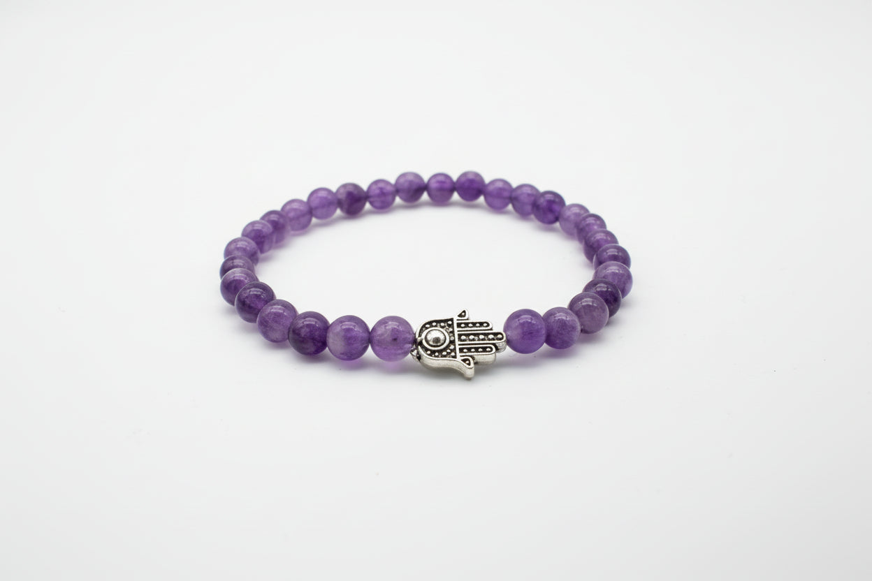 Purple beaded bracelet with a silver hamsa hand charm on a white background