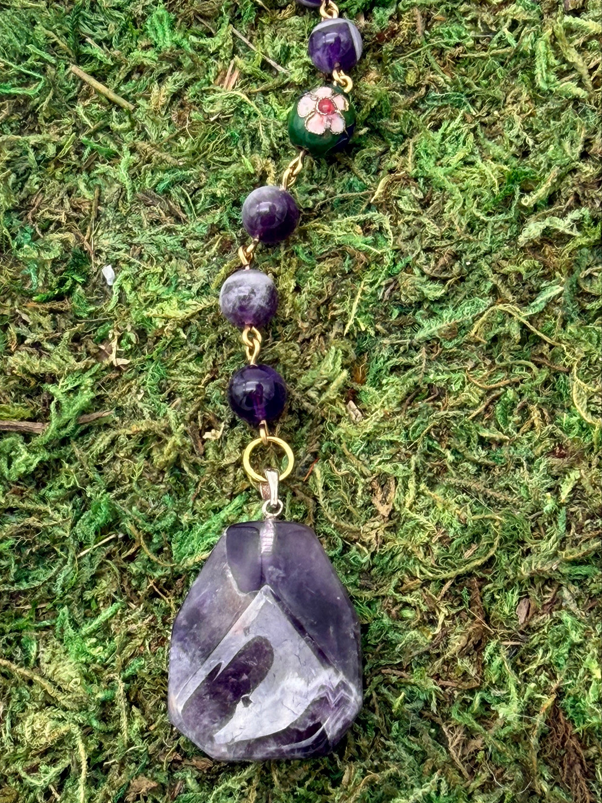 Close-up of purple and white faceted car charm, purple beads, green floral bead, and gold-toned links