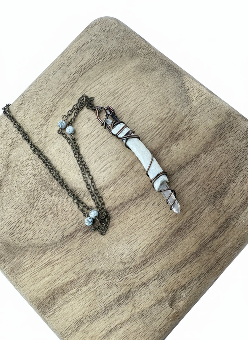 Close-up detail of the quartz point and copper wire wrapping on the deer rib bone pendant.