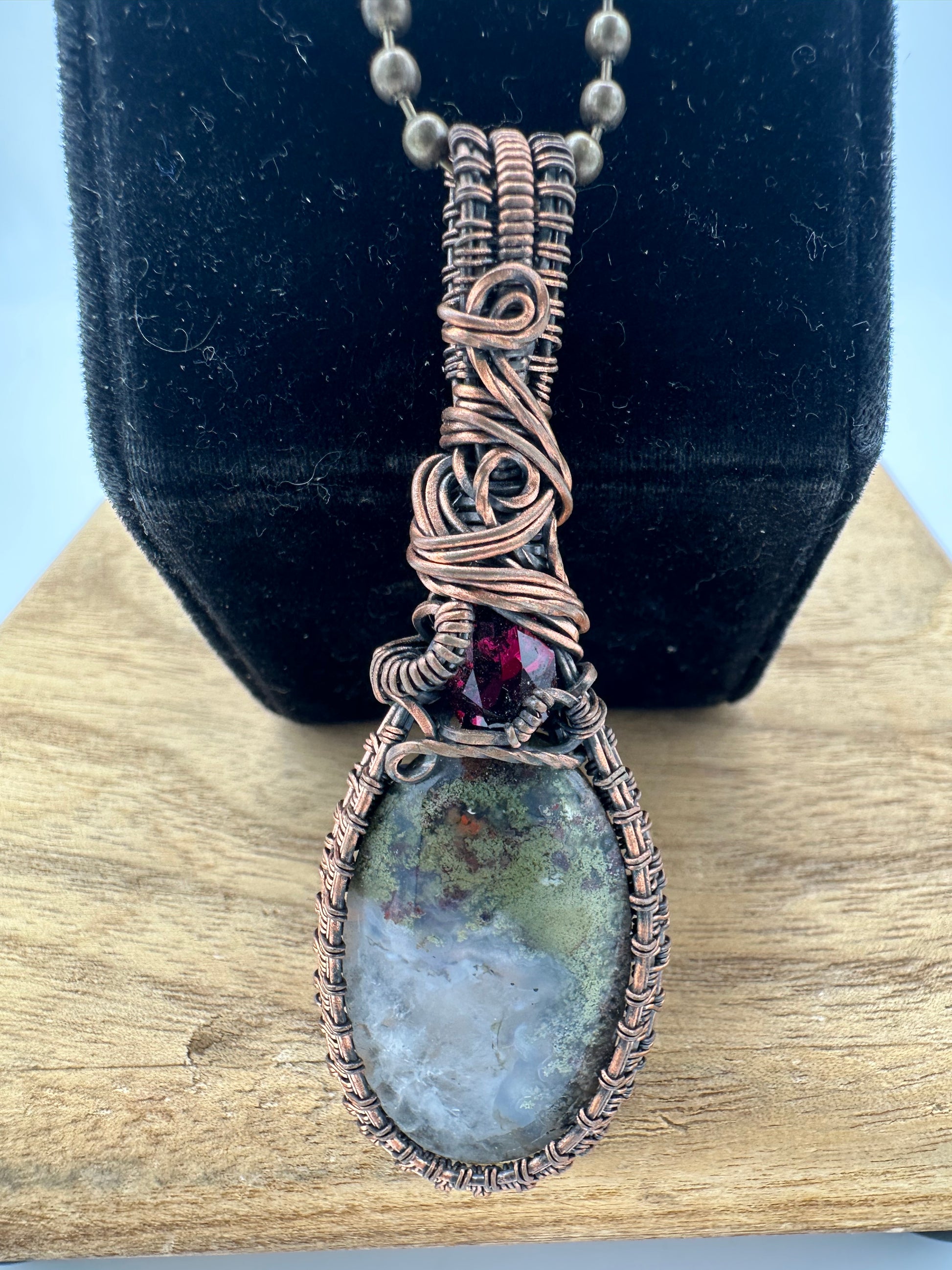 Close-up of handcrafted copper wire wrap featuring dendritic agate and garnet gemstone