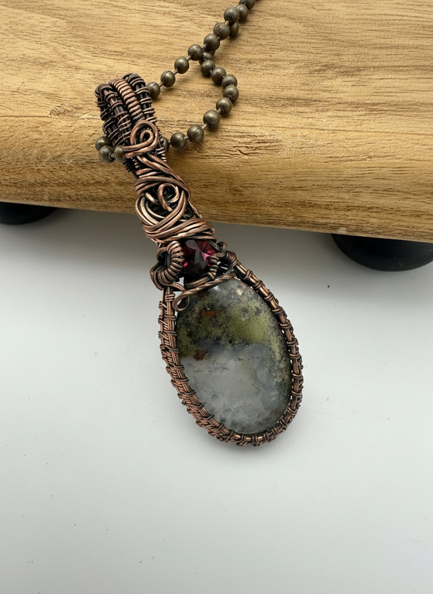 Side angle view of copper wrapped dendritic agate and garnet gemstone pendant