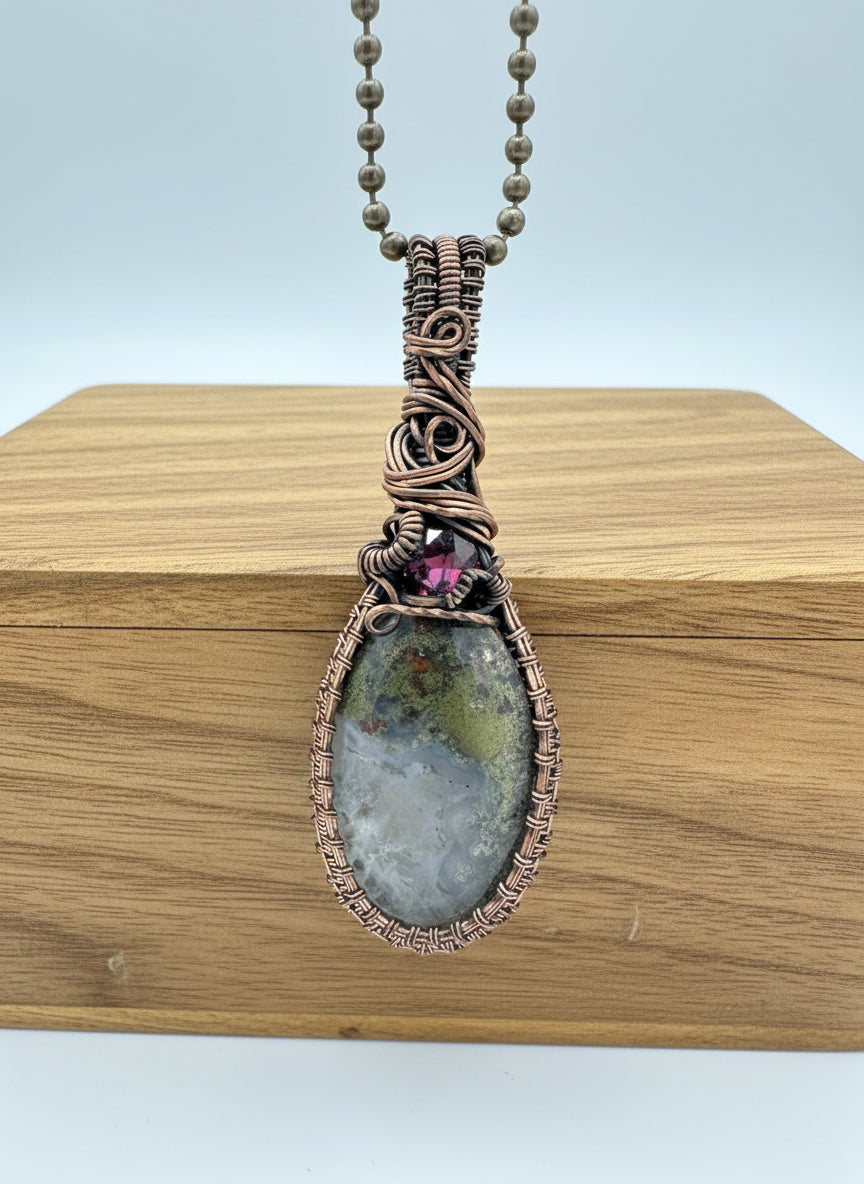 Front view of dendritic agate pendant with 3.62ct garnet wrapped in copper on 30 inch chain