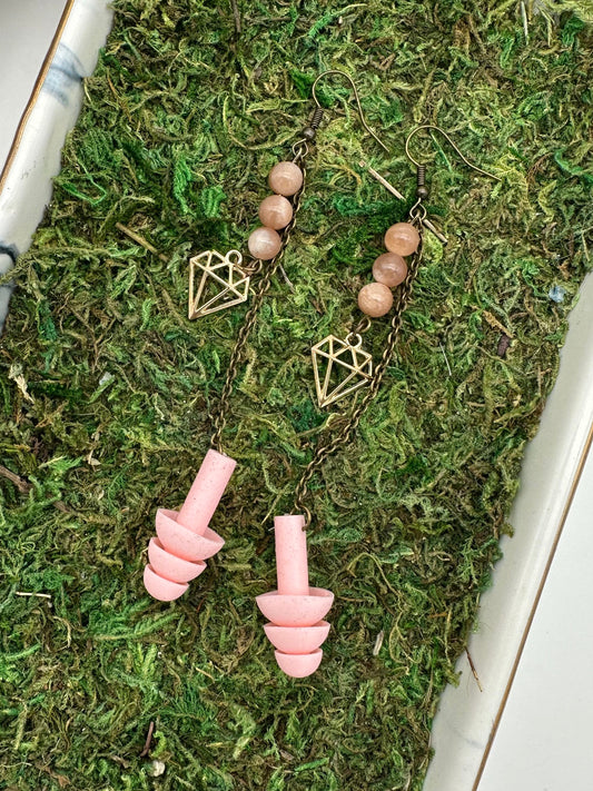 Pink earbuds and necklace on a bed of green moss in a white container.