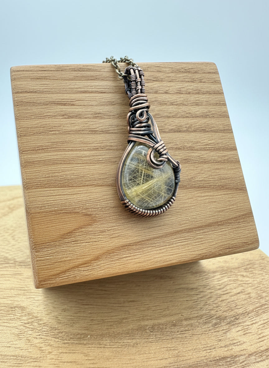 Front view of a hand-wrapped golden rutile quartz pendant in copper on an 18-inch brass chain.