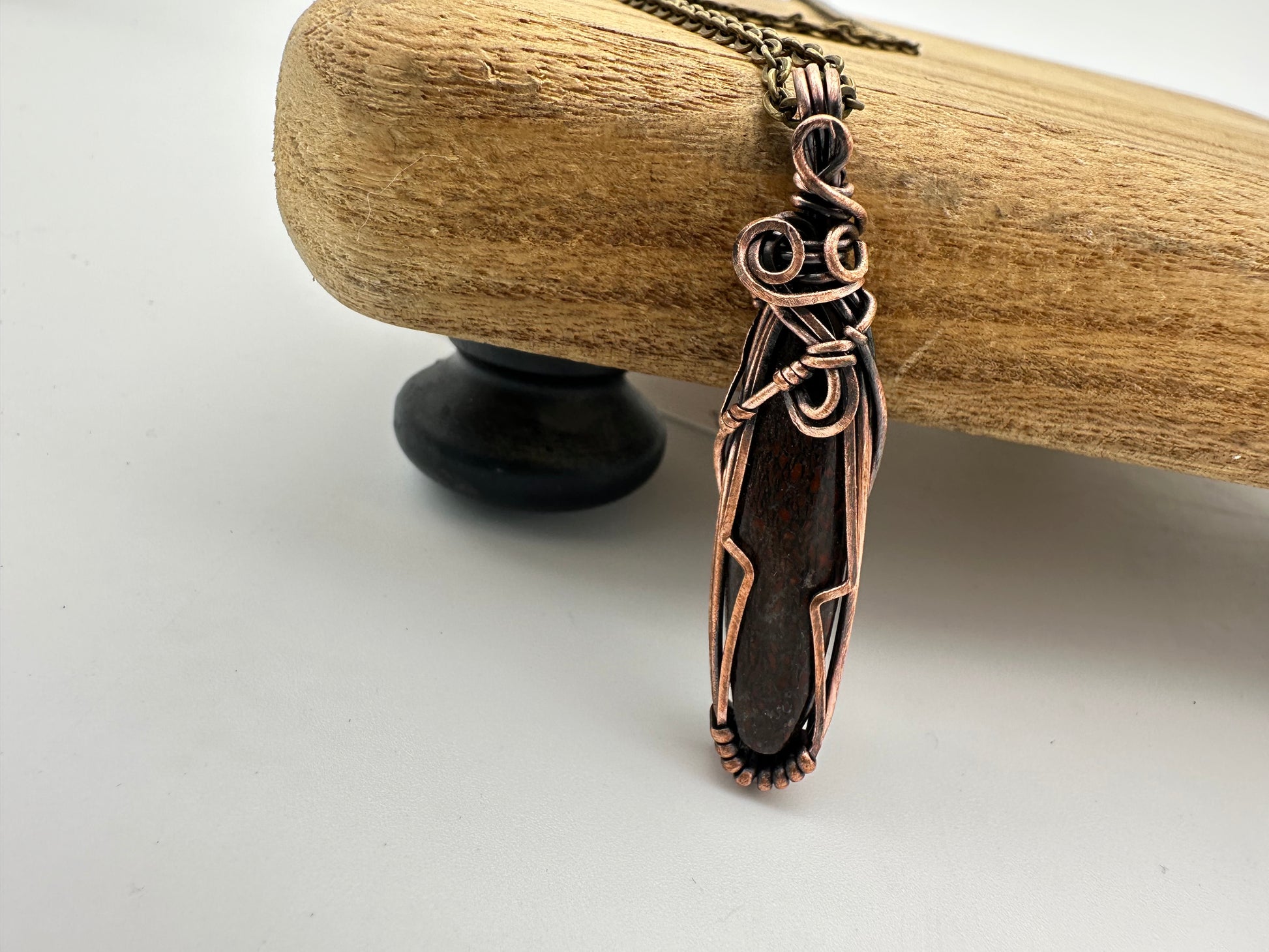 Close-up of the red dinosaur bone cabochon highlighting fossil patterns and copper wirework.