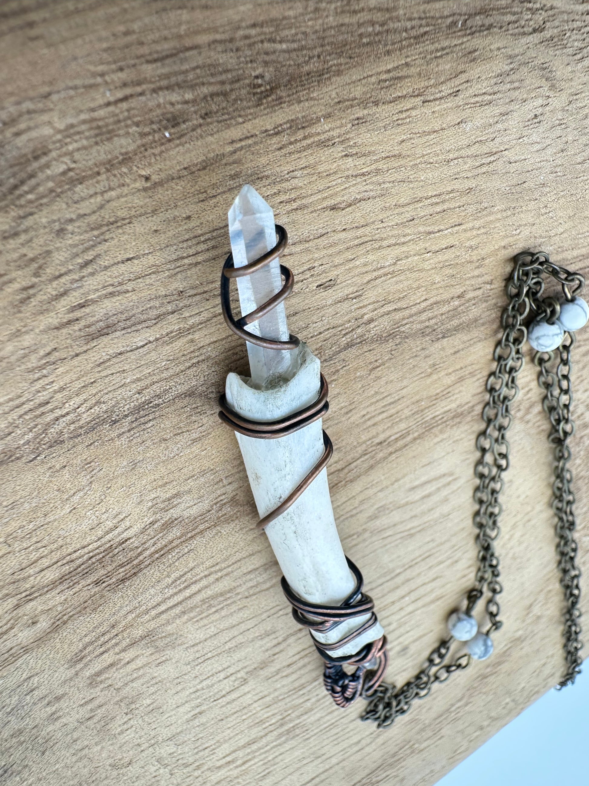 Close-up detail of the quartz point and copper wire wrapping on the deer rib bone pendant