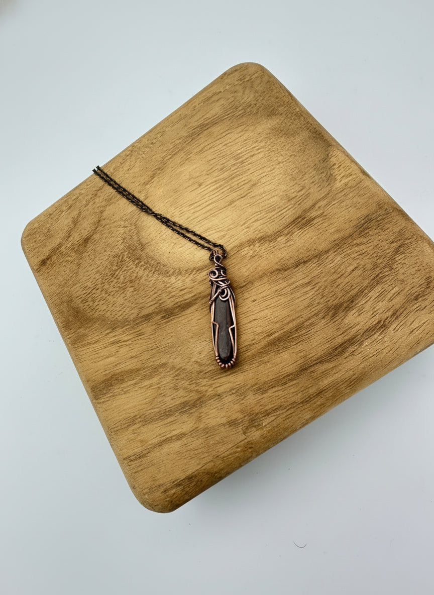 Hand-wrapped red dinosaur bone pendant in copper on a 22-inch brass chain, front view
