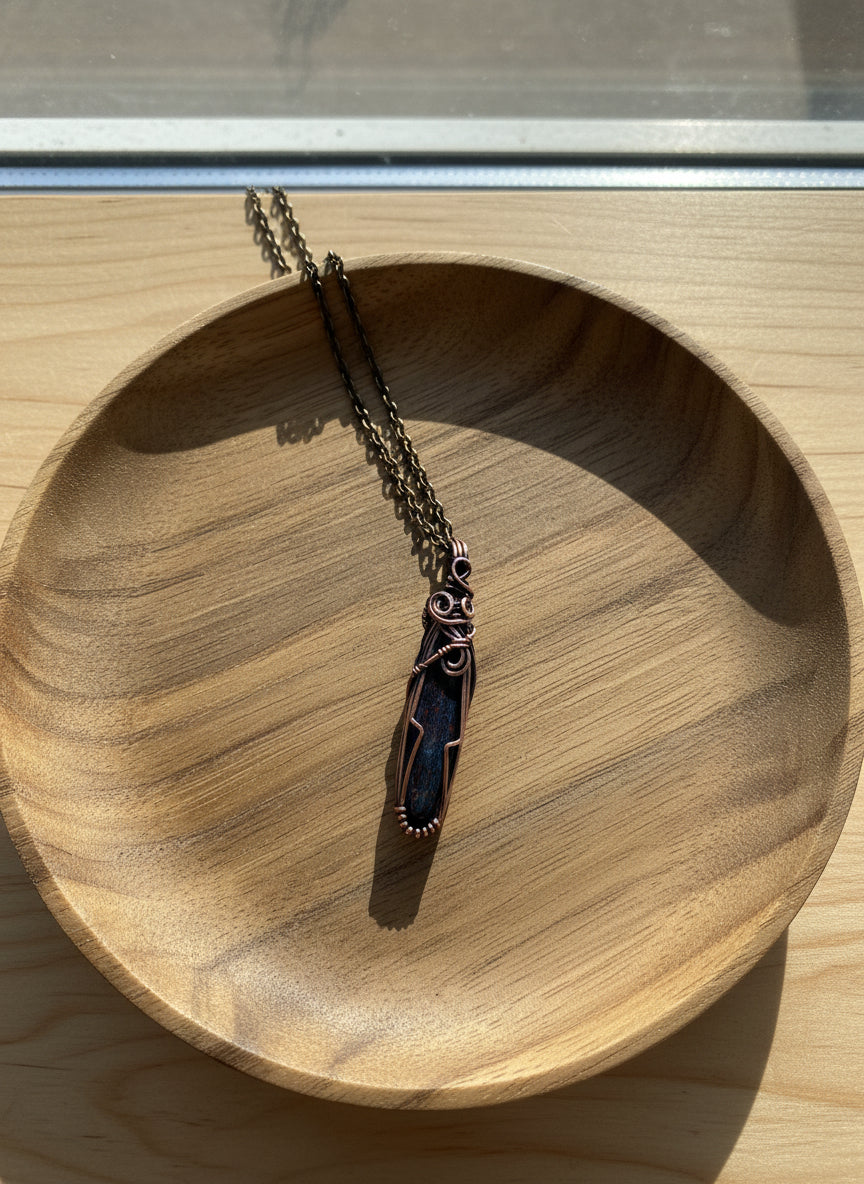 Side angle of a copper-wrapped red dinosaur bone pendant showing wire details.