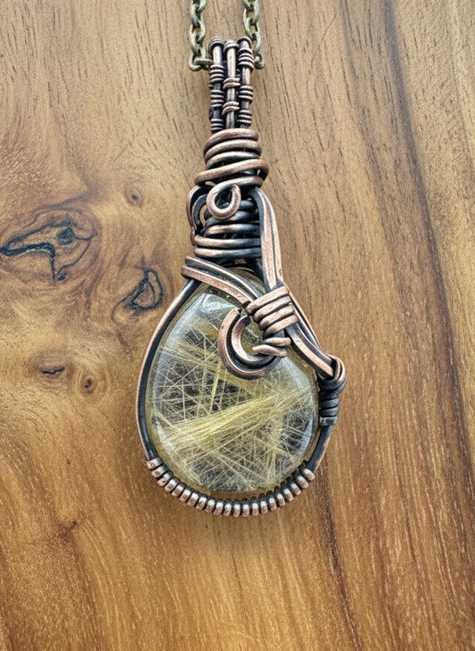 Close-up of a rutile quartz cabochon showing bright yellow rutile inclusions wrapped in copper wire