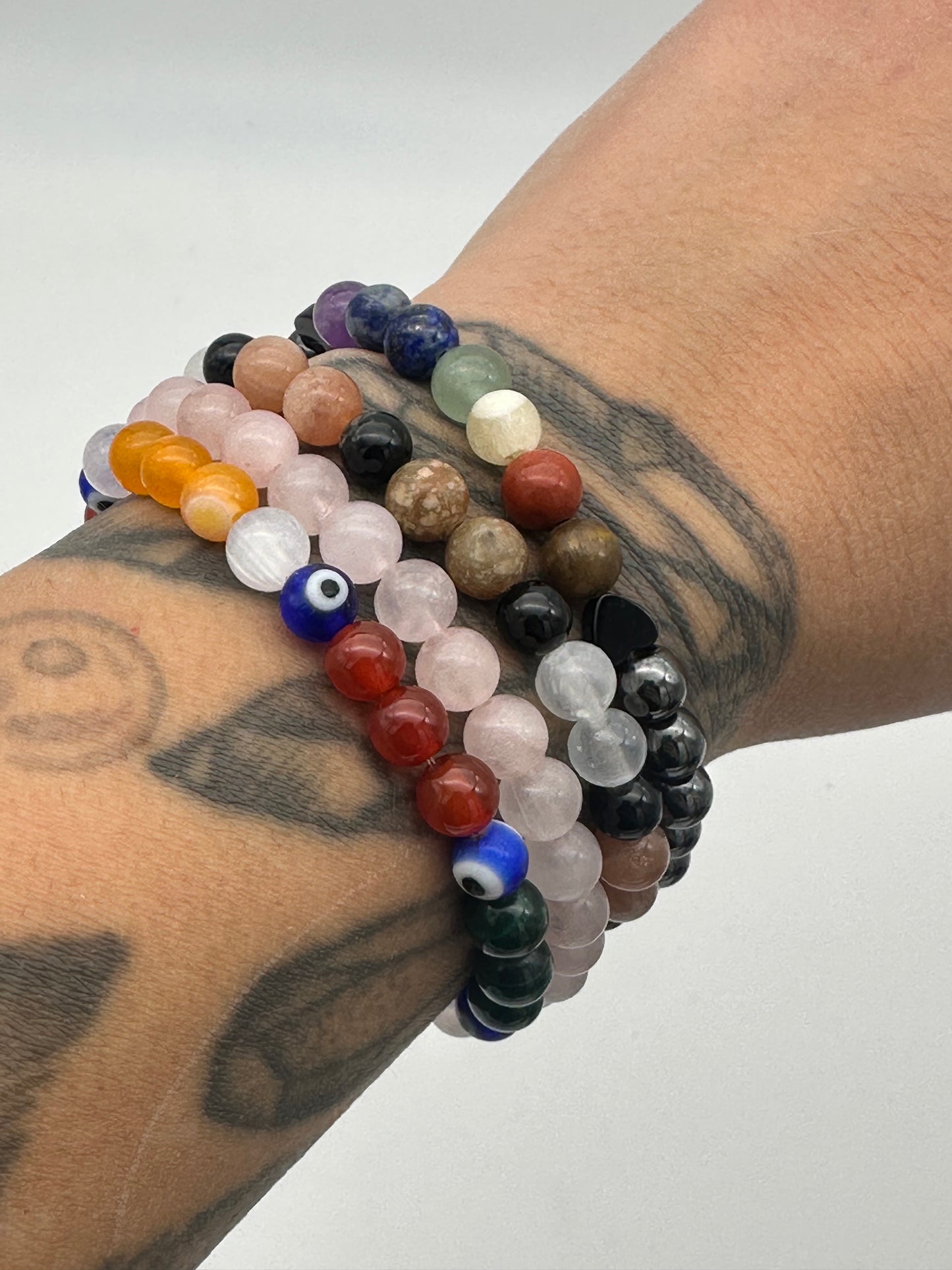 Stack of multicolored beaded bracelets on a tattooed arm against a white background